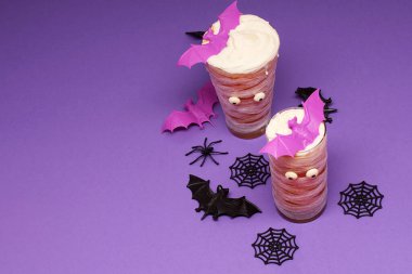 İki Cadılar Bayramı temalı içecek, yarasa karıştırıcıları, mor arka plan ve ürkütücü dekorasyonlar..