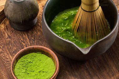 Ahşap bir yüzey üzerinde canlı yeşil çay ve toz içeren geleneksel bir kibrit çay çırpma sahnesi.