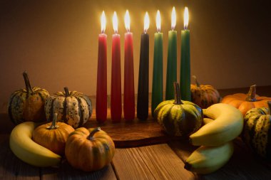 Kwanzaa. Afrika bayramı Kwanzaa yedi mum ve balkabağı süslemesiyle. Yedi mum, kırmızı, siyah ve yeşil, doğal ahşap arka planda..