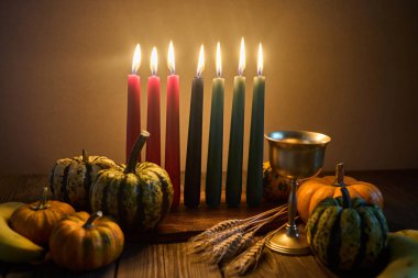 Kwanzaa. Afrika bayramı Kwanzaa yedi mum ve balkabağı süslemesiyle. Yedi mum, kırmızı, siyah ve yeşil, doğal ahşap arka planda..