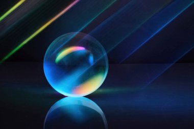 Karanlık bir zemin üzerinde renkli ışık huzmeleri olan parlak bir küre, fütüristik ve canlı bir atmosfer yaratıyor..