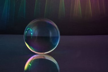 Prizmatik renkleri yansıtan camdan bir küre, karanlık, atmosferik bir arkaplan üzerine kurulmuş..