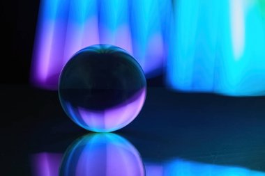 Parlayan bir cam küre, parlak mavi ve mor ışıkları karanlık bir ortamda yansıtıyor..