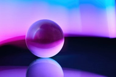 Pürüzsüz bir yüzeyde canlı mor ve mavi renkleri yansıtan bir cam küre..