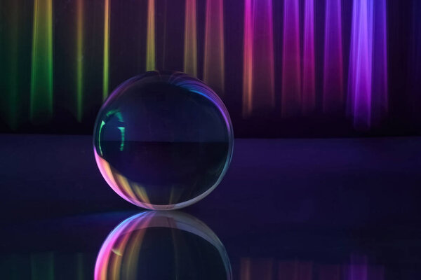 A glass sphere reflects vibrant rainbow lights against a dark background.