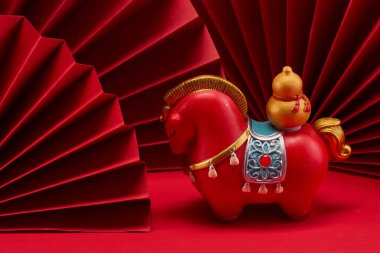 Kırmızı renkli, altın ve mavi aksanlı canlı bir at heykelciği, katlanmış kırmızı kağıt arka planda..