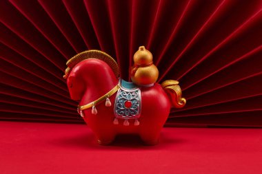 Kırmızı kağıt fanlar önünde kırmızı arkaplanda bir atın heykeli..