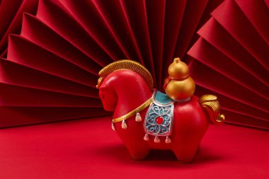 Kırmızı kağıt fanlar önünde kırmızı arkaplanda bir atın heykeli..