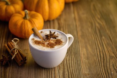 Tarçınlı balkabağı aromalı latte. Kabaklarla çevrili, ahşap bir masada..