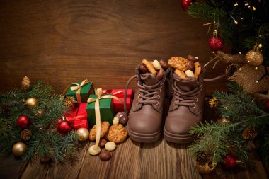 Kurabiye ve fındık dolu kahverengi çizmeler, hediyeler ve Noel süsleriyle çevrili..