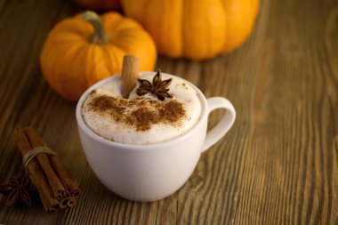 Tarçın ve yıldız anasonlu sıcak bir latte, kabaklarla çevrili, ahşap bir masada..