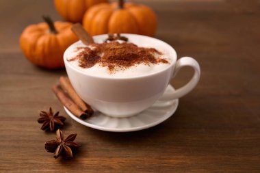 Balkabaklarıyla çevrili, ahşap bir masada tarçınlı, sade bir latte..