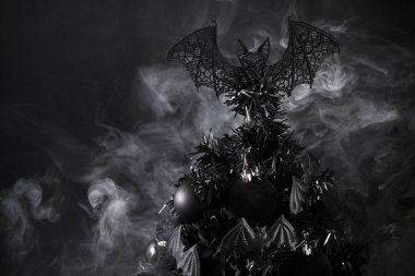 Karanlık süslemelerle süslenmiş ve gizemli bir atmosfer için sisle çevrili siyah bir Noel ağacı..
