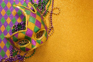 Parlayan Mardi Gras maskesi, palyaço desenli ve pırıl pırıl altın bir arka planda şenlikli boncuklar.