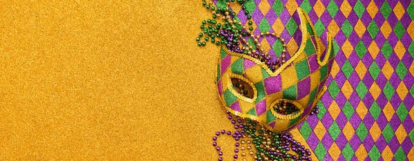 Mardi gras palyaço maskesi, altın parıltılı arkaplanda renkli boncuklar.