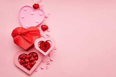 Kalp şeklinde hediye kutuları ve pembe arka planda küçük kalpler. Aşkı ve kutlamayı simgeliyor.