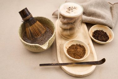 Köpüklü hojicha latte ve hafif arka planda çay seremonisi araçları