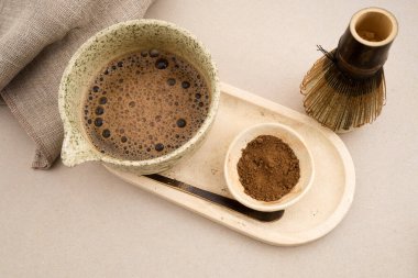 Seramik bir chawan 'da Hojicha içeceği. Tepside çay tozu ve bambu çırpısı var.