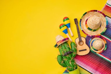 Sarı arka planda kaktüs, sombrero, marakas ve gitarlı renkli Meksika Fiesta dekorasyonları.