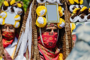 Puebla, Meksika 28 Eylül 2025: Huey Atlixcayotl festivalinde yerel kültürü temsil eden kırmızı ve altın desenli bir yüz eşarbı takan geleneksel giyinmiş bir dansçının yakın plan portresi.