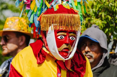 Puebla, Meksika 8 Eylül 2025: Kırmızı ahşap maske ve arka planda canlı renkler içeren püsküllü başlıklı ve kağıt şeritli bir maskeli dansçının yakın çekimi