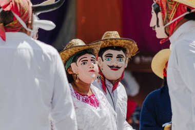 Puebla, Meksika 28 Eylül 2025: İnsan yüzü maskeli, hasır şapkalı ve geleneksel beyaz kostümlü dansçıların yakın çekimi, kültürel bir kutlamaya katılım