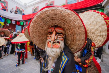 Huey Atlixcayotl kutlamasında büyük bir hasır şapka takan geleneksel maskeli ve beyaz sakallı bir dansçının yakın çekimi..