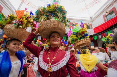 Puebla, Meksika 9 Eylül 2025: Başında büyük bir çiçek sepetiyle gülümseyen Meksikalı kadın, geleneksel bir şenliği diğer insanlarla kutluyor..