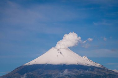Yoğun mavi gökyüzüne karşı bir duman sütunu yayarak, kar kaplı Popocatpetl Volkanı 'nın yakın plan görüntüsü.