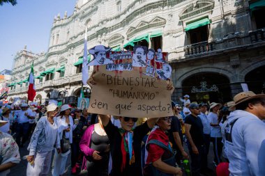 Puebla, Meksika; 11-15-25: Meksika 'nın Puebla kentindeki kırmızı koloni mimarisinin kuşattığı dar bir sokakta yürüyen yoğun protestocu kalabalığı.