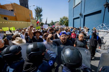 Puebla, Mxico; 11-15-25: Protestocular bağırıp yumruklarını kaldırarak Puebla, Meksika sokaklarında isyan kalkanları olan bir grup polis memuruyla karşı karşıya geldiler.