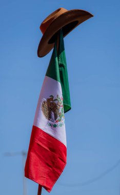 Puebla, Mxico; 11-15-25: Puebla 'daki sivil protestonun güçlü bir sembolü olan mavi gökyüzüne doğru dalgalanan Meksika bayrağının üzerine yerleştirilmiş bir kovboy şapkası..