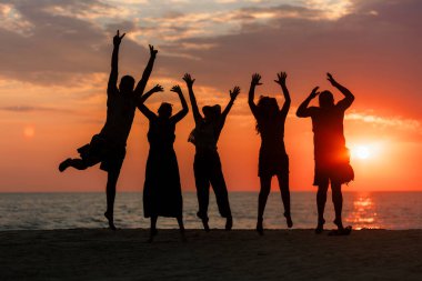 Sahilde sıcak ve renkli bir yaz günbatımında neşeyle atlayan beş kişinin silueti..