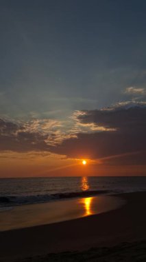 Güneşin yoğun bir şekilde ıslak sahilde yansıttığı ve zıt kara bulutların olduğu muhteşem bir gün batımı..