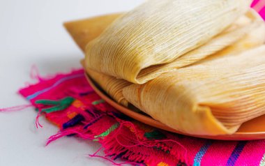 Sıcak Meksika tamalelerini saran kuru mısır kabuğu dokusunun detaylı bir yakın çekimi, kırsal ve geleneksel kültür ortamında servis edilir.