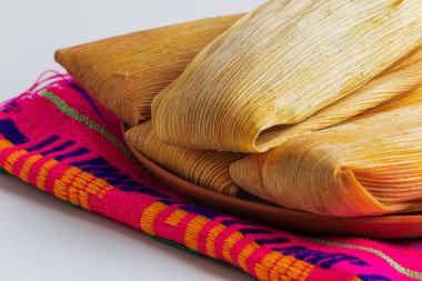 Sıcak Meksika tamalelerini saran kuru mısır kabuğu dokusunun detaylı bir yakın çekimi, kırsal ve geleneksel kültür ortamında servis edilir.