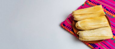 Beyaz arka planda geleneksel Meksika gastronomisi ve kültürel kutlamaları temsil eden renkli bir zanaatkar peçetesine birkaç tane tamale yerleştirildi..