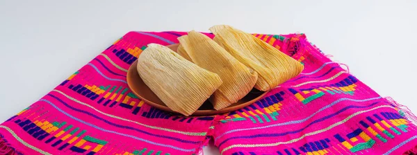 Beyaz arka planda geleneksel Meksika gastronomisi ve kültürel kutlamaları temsil eden renkli bir zanaatkar peçetesine birkaç tane tamale yerleştirildi..