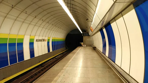 Platform of metro station Hloubetin of Prague metro line B. The station is decorated with blue, green, and yellow strips. On the ground is reflection of fluorescent lamp hanging from the ceiling. There are no people waiting for metro at the moment.