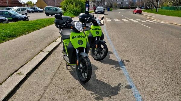 Aracı paylaşan BeRider şirketinin motosikletleri park yeri yolu ve kaldırımı olan ve arka planda yaya geçidi olan bir otopark..