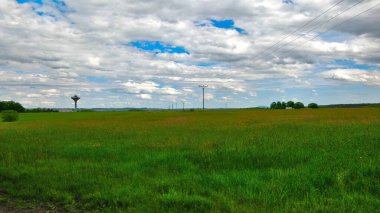 Elektrik şebekesi yamaçlı ve arka planda su kulesi olan bir alan güzel bir bahar gününde. Mavi gökyüzündeki beyaz bulutlar bu Güney Bohem manzarasını çok rahatlatıyor..