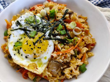 Sebzeli, mantarlı, yumurtalı, yosunlu ve siyah susamlı Japon usulü pilav. Tabak beyaz kâsede servis edilir..