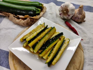 Beyaz tabakta servis edilen kırmızı biberli kabaktan yapılmış bir tabak. Sol üstte iki tane kabak ve sağ üstte iki parça sarımsaklı kırmızı biber var..