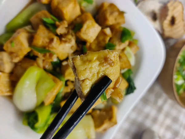 豆腐干 豆腐和葱葱做的一道菜上面 夹着几根筷子 后面的盘子模糊不清 — 图库照片