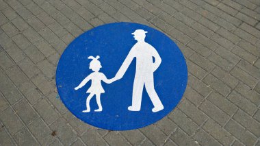 Kaldırıma basılmış mavi halkalı bir kızı tutan şapkalı bir adamın sembolü. Burası bir yürüyüş alanı. Kaldırımlar gri ve görüntü beyaz..