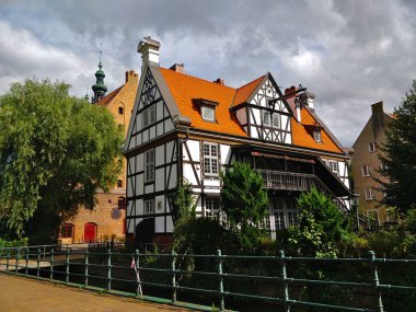 Gdansk, Polonya - 26 Ağustos 2021: Gdansk şehir merkezinin kıyısındaki eski tarihi ev ahşap kirişli beyaz cephe ve bulutlu havalarda kırmızı çatı.