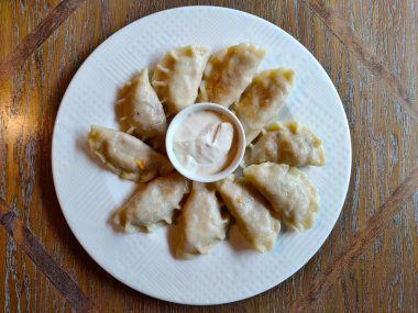 Geleneksel Polonya pirogu beyaz tabakta servis ediliyor. Tabağın ortasındaki küçük kasede mayonez var..