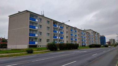 Kladno, Çek Cumhuriyeti - 19 Eylül 2021: Bulutlu havada boş geniş yolun kenarında duran mavi balkonlu dört katlı gri apartman bloğu.