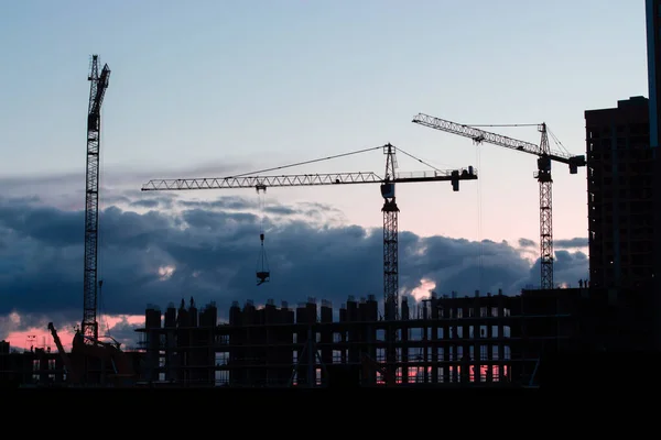 Black silhouette of a construction crane, dramatic twilight sky. Residential building construction, night photography