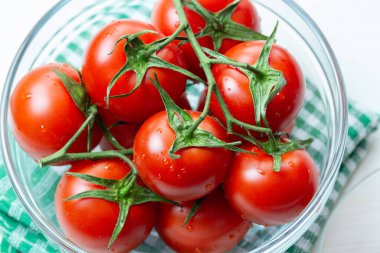 Şeffaf cam kasede su damlaları olan kırmızı domates dalıyla, üst manzara. Olgun doğal organik sebze domatesleri.